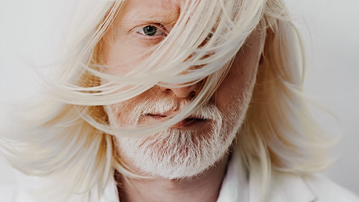 An albino man with a white beard and gorgeous white hair, wearing a white jacket on a white background